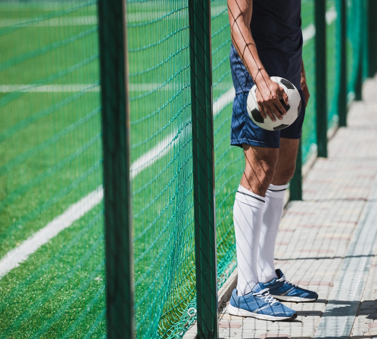 cropped shot of soccer player holding ball while standing near soccer pitch