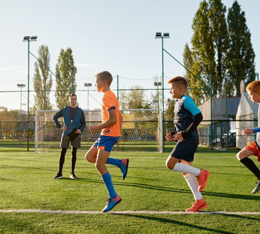 Kids practicing soccer on grass field under football coach control